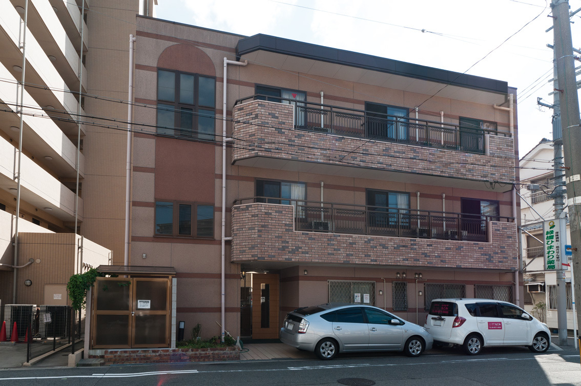 介護施設の3階建て建物外観。玄関前に駐車スペースがある。