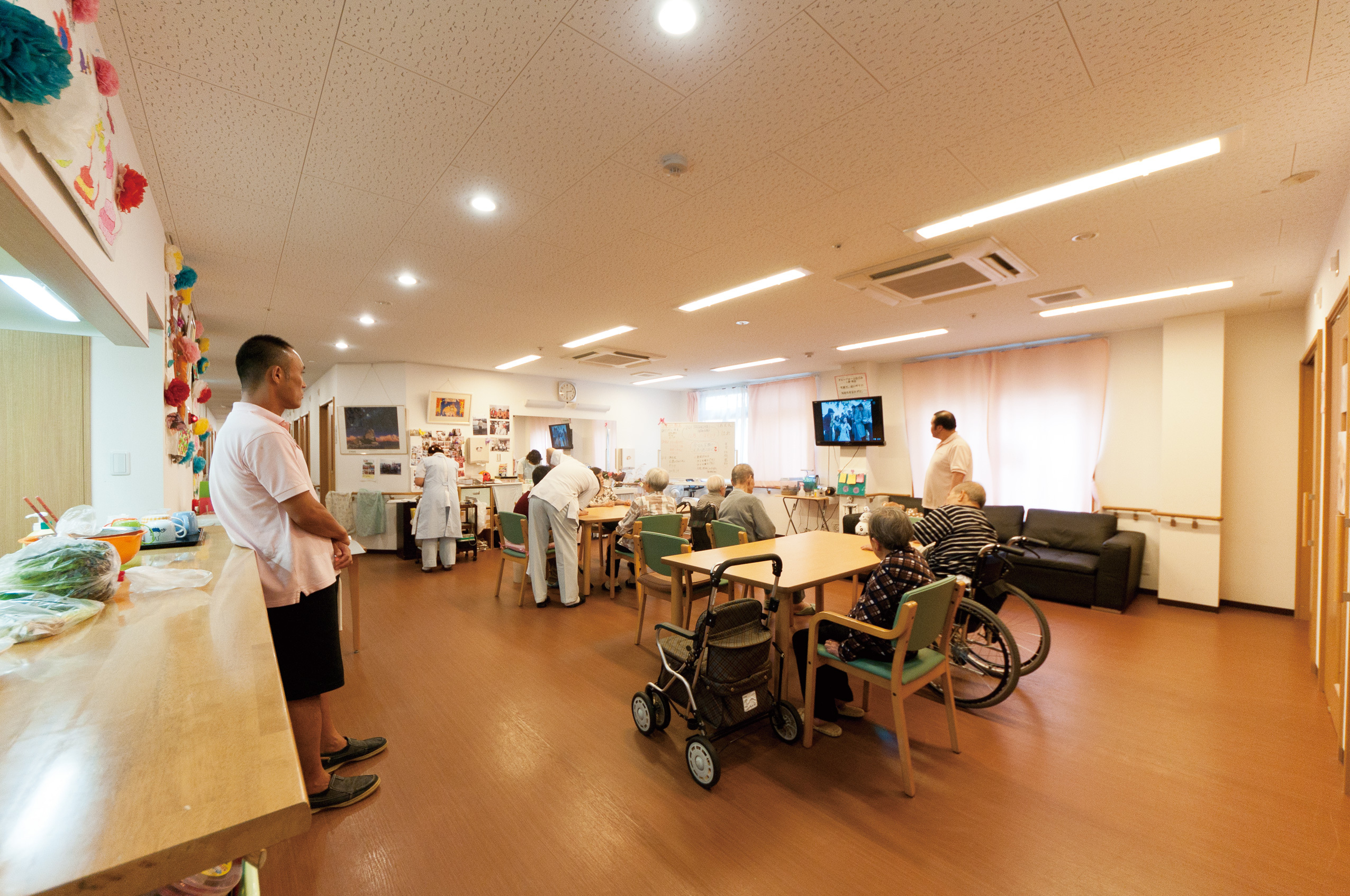 介護施設の共用スペース。入居者と職員が日常生活を送る広々とした明るいリビング・談話室。