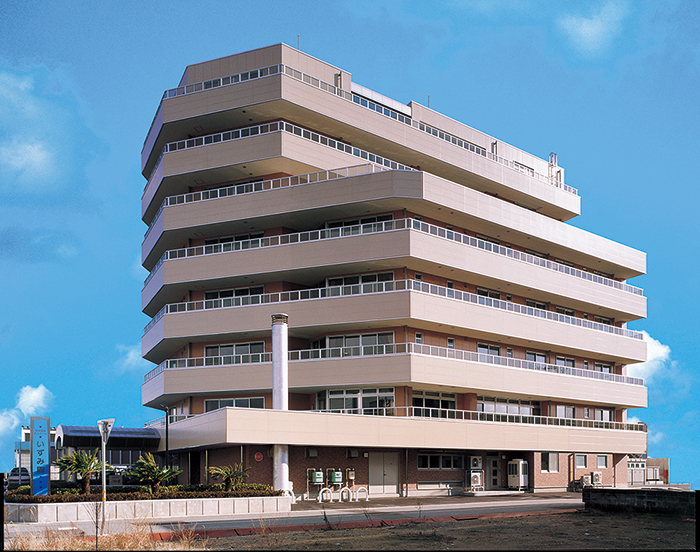 海辺に立つ円形の介護施設の建物全景。複数階の窓が特徴的。