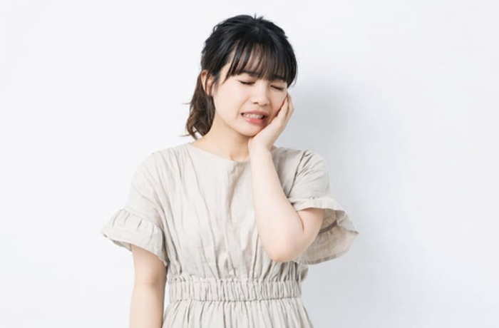 歯の痛みや虫歯で頬を押さえる女性のイメージ写真