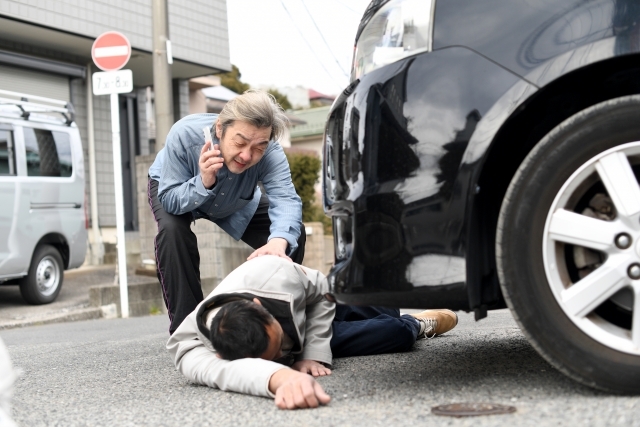 交通事故で車の前で横たわる男性